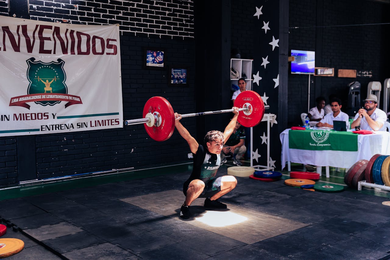 Athlete executing a snatch lift at a weightlifting competition indoors.
