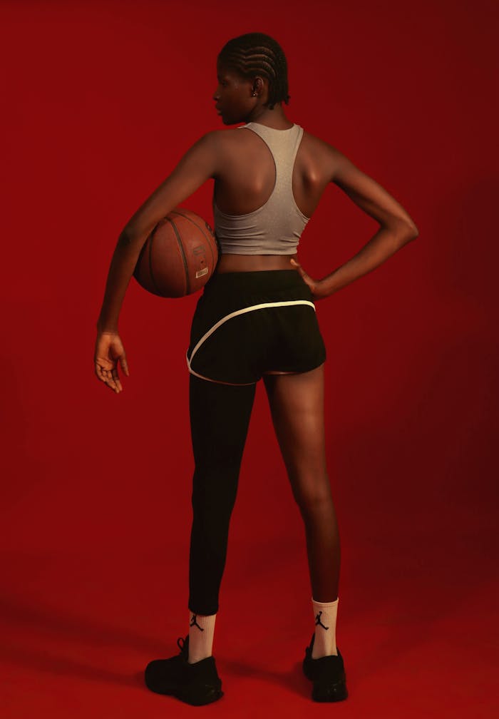 Female athlete with basketball on vibrant red backdrop, showcasing strength and focus.
