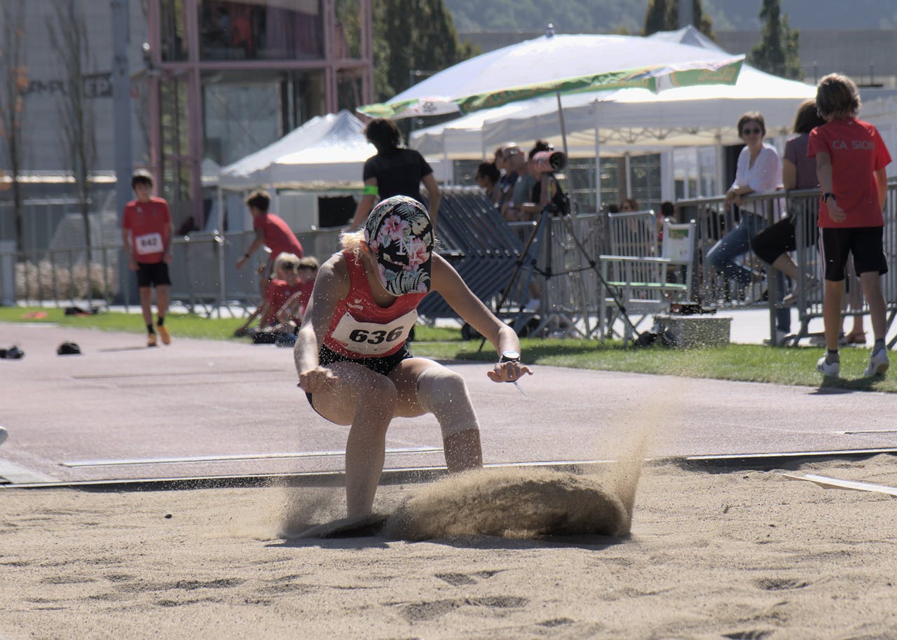 Female athlete captured mid-landing in the long jump event during a sunny sports meet.